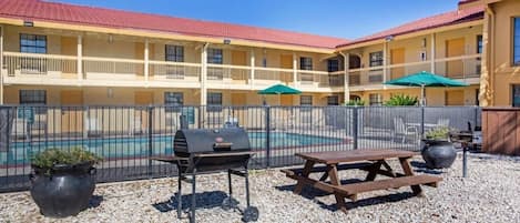 A poolside area with a barbecue grill, picnic table, and umbrellas.