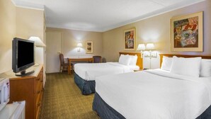 A hotel room with two beds, a desk, a chair, a television, and artwork on the walls.