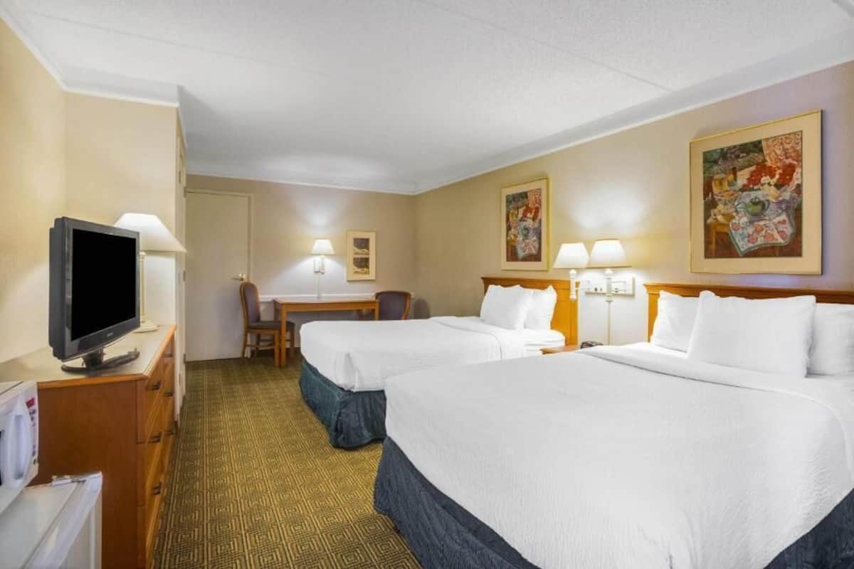 A hotel room with two beds, a desk, a chair, a television, and artwork on the walls.