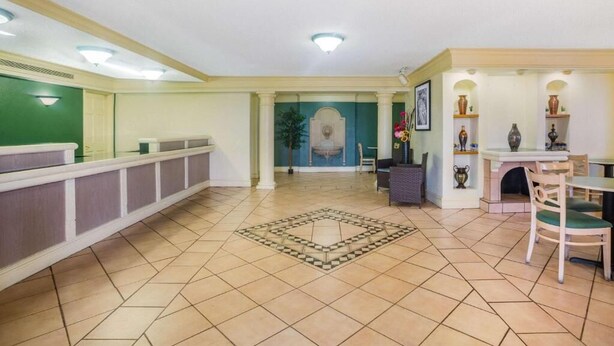 A hotel lobby with a reception desk, a dining area, and a decorative wall.