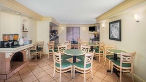 A dining area with multiple tables and chairs, a kitchen area with a stove, and a television mounted on the wall.