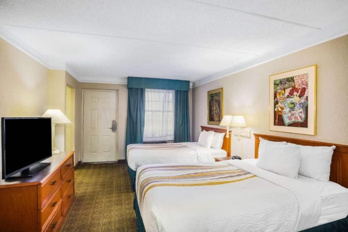 A hotel room with two beds, a television, a desk, and a painting on the wall.