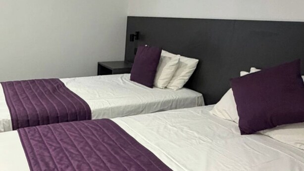 Two beds with white linens and purple accents, a dark headboard, and a small bedside table. - Commercial Hotel - Standard Twin Room Shared (Middlesbrough)
