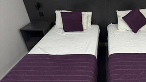 Two single beds with white and purple bedding, a dark headboard, and a small bedside table. - Commercial Hotel - Standard Twin Room Shared (Middlesbrough)