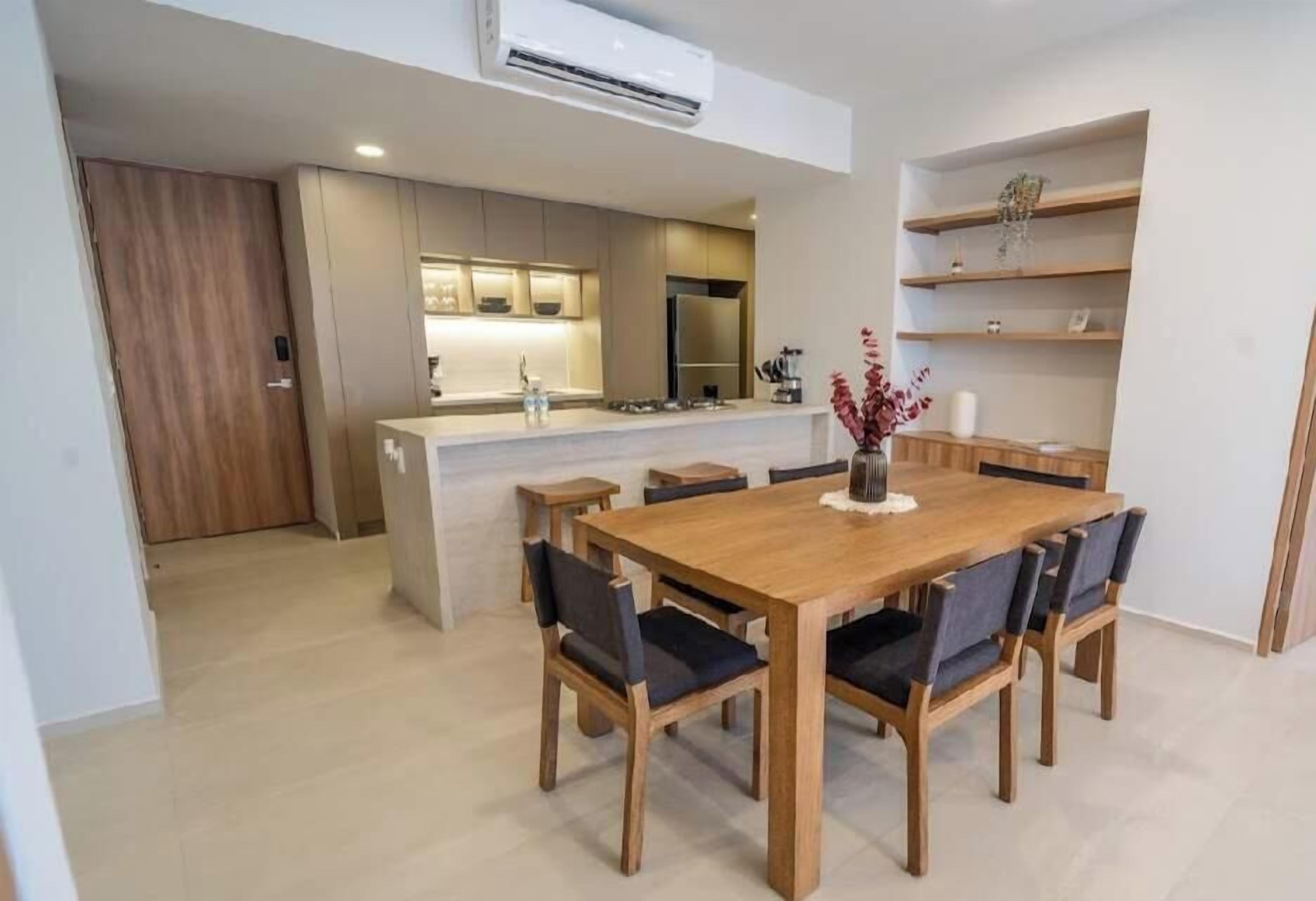 Uma cozinha moderna com eletrodomésticos embutidos, um espaço de refeições com mesa e cadeiras de madeira e uma pequena ilha com pia.
