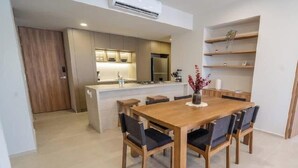 Een moderne keuken met inbouwapparatuur, een eethoek met een houten tafel en stoelen, en een klein keukeneiland met een spoelbak.