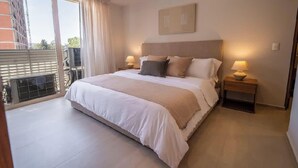 Een hotelkamer met een groot bed, twee nachtkastjes met lampen, een uitzicht naar buiten en een raam met gordijnen.