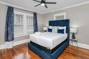 Un dormitorio con cama, cortinas, ventilador de techo y mesita de noche.