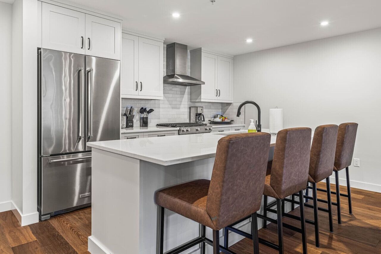 A modern kitchen with stainless steel appliances, a central island with bar stools, and white cabinetry.