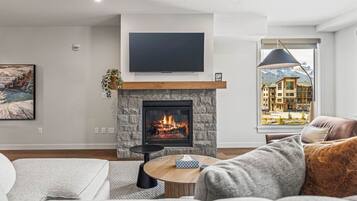 A living room with a fireplace, a flat-screen TV, and a view of a building through a window.