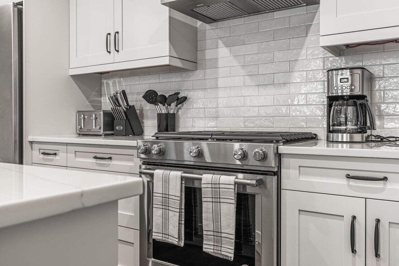 A kitchen with white cabinets, a stainless steel stove, a coffee maker, and a toaster.