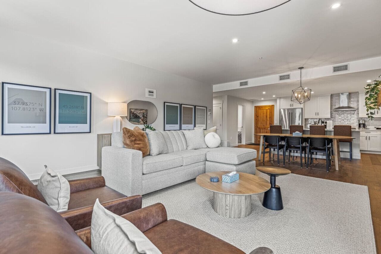 Ein modernes Wohnzimmer mit grauem Sofa, Couchtisch und Essbereich mit Holztisch und Stühlen.