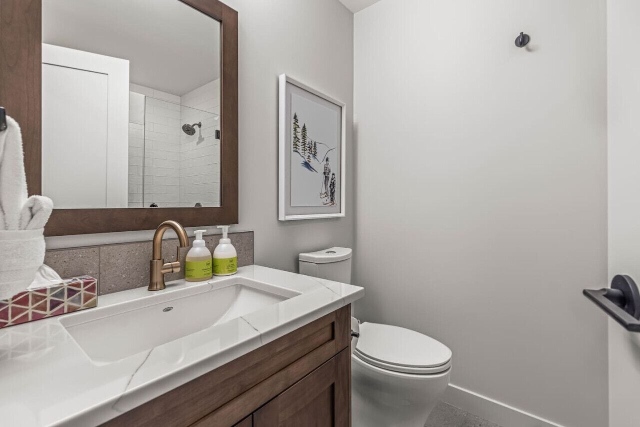 A modern bathroom with a white sink, a large mirror, a framed artwork, and a toilet.