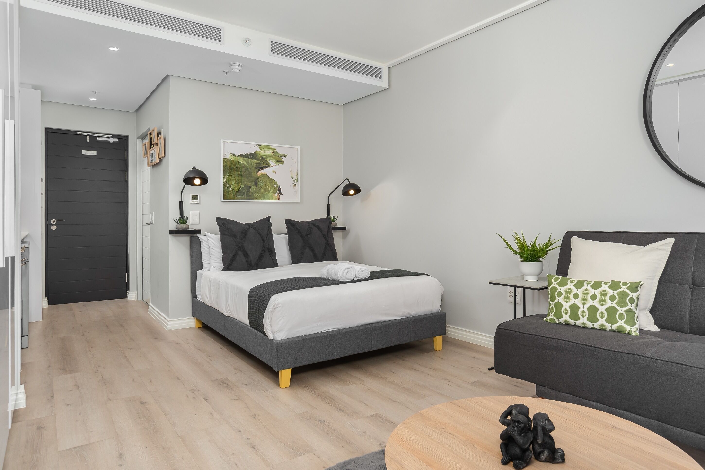 A modern bedroom with a bed, bedside tables, a sofa, a round coffee table, and a potted plant.