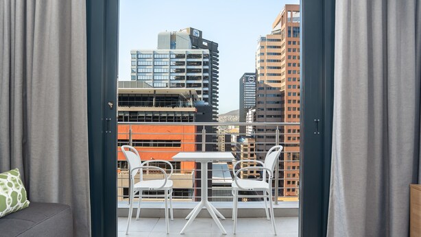 Ein Balkon mit Tisch, Stühlen, einer Couch und Blick auf Stadtgebäude.