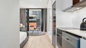 Ein modernes Hotelzimmer mit Küche, einem Essbereich mit Tisch und Stühlen, einem Bett und Blick auf die Stadtlandschaft.