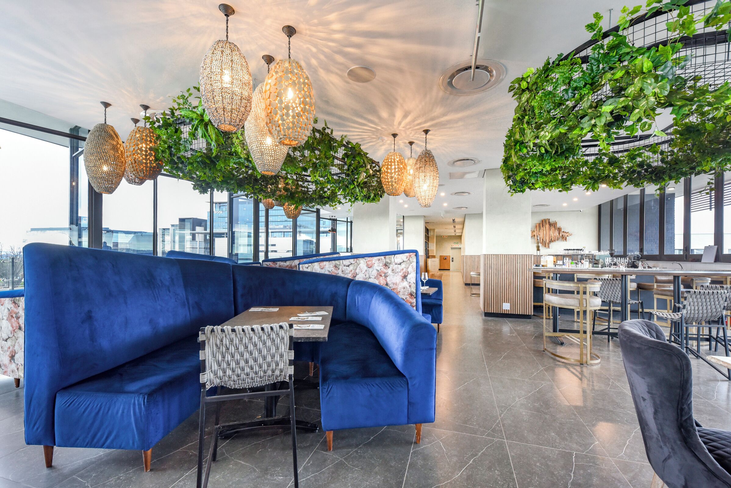 Uma área de estar moderna com um sofá azul, lustres de cristal pendurados e uma instalação com folhagem verde.