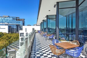 A rooftop terrace with checkered flooring, glass railings, and outdoor seating. - One Rosebank | A Little City Romance (Johannesburg)