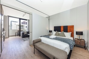 Ein modernes Schlafzimmer mit einem großen Bett, Nachttischen, einer Bank und Blick ins Freie.