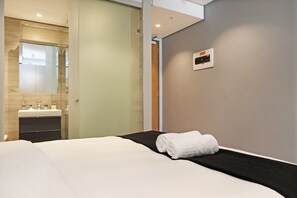 Ein Hotelzimmer mit Bett, schwarzem Kopfteil, einer fest montierten Bedienkonsole und einem Badezimmer mit Spiegel und Waschbecken.