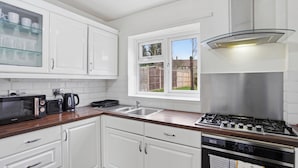 A kitchen with white cabinets, a microwave, a kettle, a stove, and a window with a view of a backyard. - Contractor/Family Friendly 4 Bedroom House w/WIFI & Free Parking (West Bromwich)