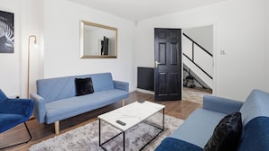 A living room with a sofa, a coffee table, a mirror, and a door leading to a staircase. - Contractor/Family Friendly 4 Bedroom House w/WIFI & Free Parking (West Bromwich)