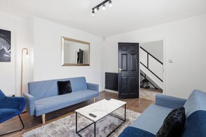 Ein Wohnzimmer mit einer Couch, einem Couchtisch, einem Spiegel und einer Tür zu einer Treppe.