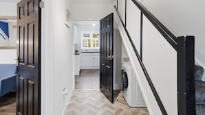 A hallway leading to a kitchen with a washing machine, a bed, and a staircase. - Contractor/Family Friendly 4 Bedroom House w/WIFI & Free Parking (West Bromwich)