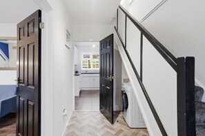 Ein Flur, der zu einer Küche mit Waschmaschine, einem Bett und einer Treppe führt.