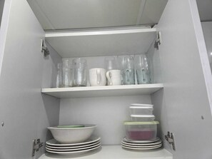 Ein Küchenschrank mit Regalen, auf denen klare Trinkgläser, weiße Tassen und gestapelte Teller stehen.