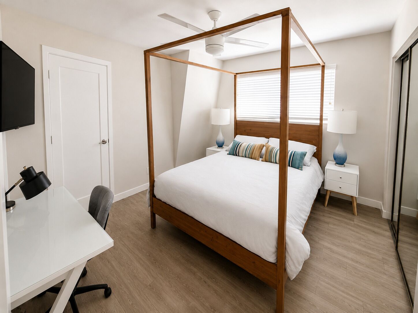 Een slaapkamer met een hemelbed, een bureau met stoel, een televisie en een plafondventilator.