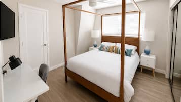 Een slaapkamer met een hemelbed, een bureau met stoel, een televisie en een plafondventilator.