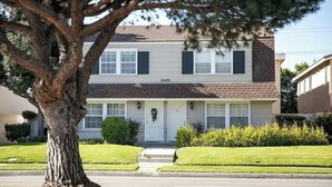 A two-story house with a brick facade, a front porch, and a tree in the foreground. - Modern 2BR Townhome in South Torrance (Torrance)