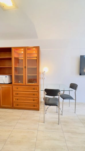 Una habitación con un armario de madera, una mesa de vidrio, dos sillas y un televisor fijado a la pared.