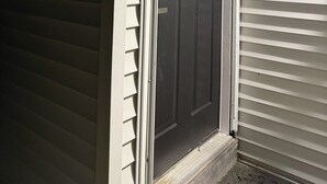 Uma casa com porta da frente escura, revestimento branco e um pequeno alpendre.