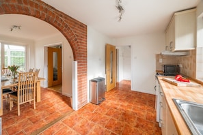 Eine Küche mit einer Ziegelbogenarchitektur, ein Essbereich mit Stühlen und einem Tisch sowie eine Küchenarbeitsplatte mit Spüle und einer roten Paprika.