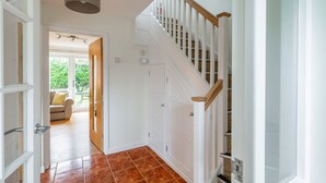 A hallway with a staircase, a door leading to a room with a sofa, and a view of the outdoors. - Swift Host | Watermeadow | Sleeps 5 | Parking | Garden | Dereham (488234) (Elsing)