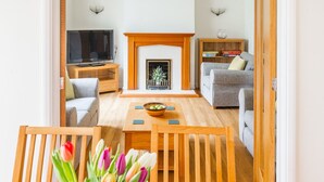 A living room with a fireplace, a television, a sofa, and a dining area with a table and chairs. - Swift Host | Watermeadow | Sleeps 5 | Parking | Garden | Dereham (488234) (Elsing)