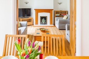 Ein Wohnzimmer mit Kamin, Fernseher, einer Couch und einem Essbereich mit Tisch und Stühlen.