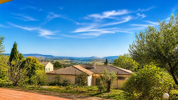 Una casa rural con tejado de tejas, rodeada de follaje y un cielo azul despejado.