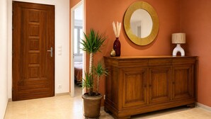 Un pasillo con una puerta de madera, una planta en maceta, un espejo y un armario.