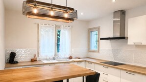 Una cocina moderna con encimera de madera, dos taburetes de bar, una lámpara colgante y una ventana con cortinas.