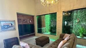 Un soggiorno con un'ampia sezione angolare, un lampadario, un televisore e una parete verde con una pianta rampicante.