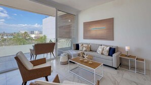 Ein modernes Wohnzimmer mit Sofa, Couchtisch und Sesseln, einem großen Fenster mit Blick auf die Stadt sowie einem minimalistischen Kunstwerk an der Wand.