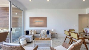 Ein modernes Wohnzimmer mit Glastür zum Balkon, einer Sofagarnitur, einem Couchtisch, Korbstühlen und einem Essbereich mit Glastisch.