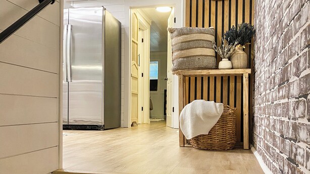 A staircase leading to a kitchen with a refrigerator, a wooden shelf with decorative items, and a wall-mounted mirror.