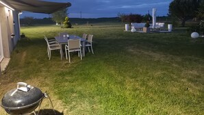 A covered patio with a table and chairs, a barbecue grill, and a view of the surrounding grassy area. - For a long weekend or a vacation in the countryside. (Thilouze)