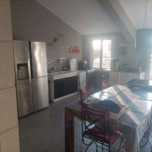 A modern kitchen with stainless steel appliances, a coffee station, and a dining area with a table and chairs. - For a long weekend or a vacation in the countryside. (Thilouze)