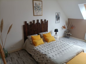 Ein Schlafzimmer mit einem hölzernen Kopfende, einem Bett mit gemusterten Textilien, einem kleinen Nachttisch und einem an der Wand hängenden Bild.