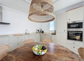 A kitchen with a round wooden table, wicker chairs, a woven pendant light, and built-in appliances. - Mb.b53 - Beachfront Penthouse With Sea Views (Estepona)